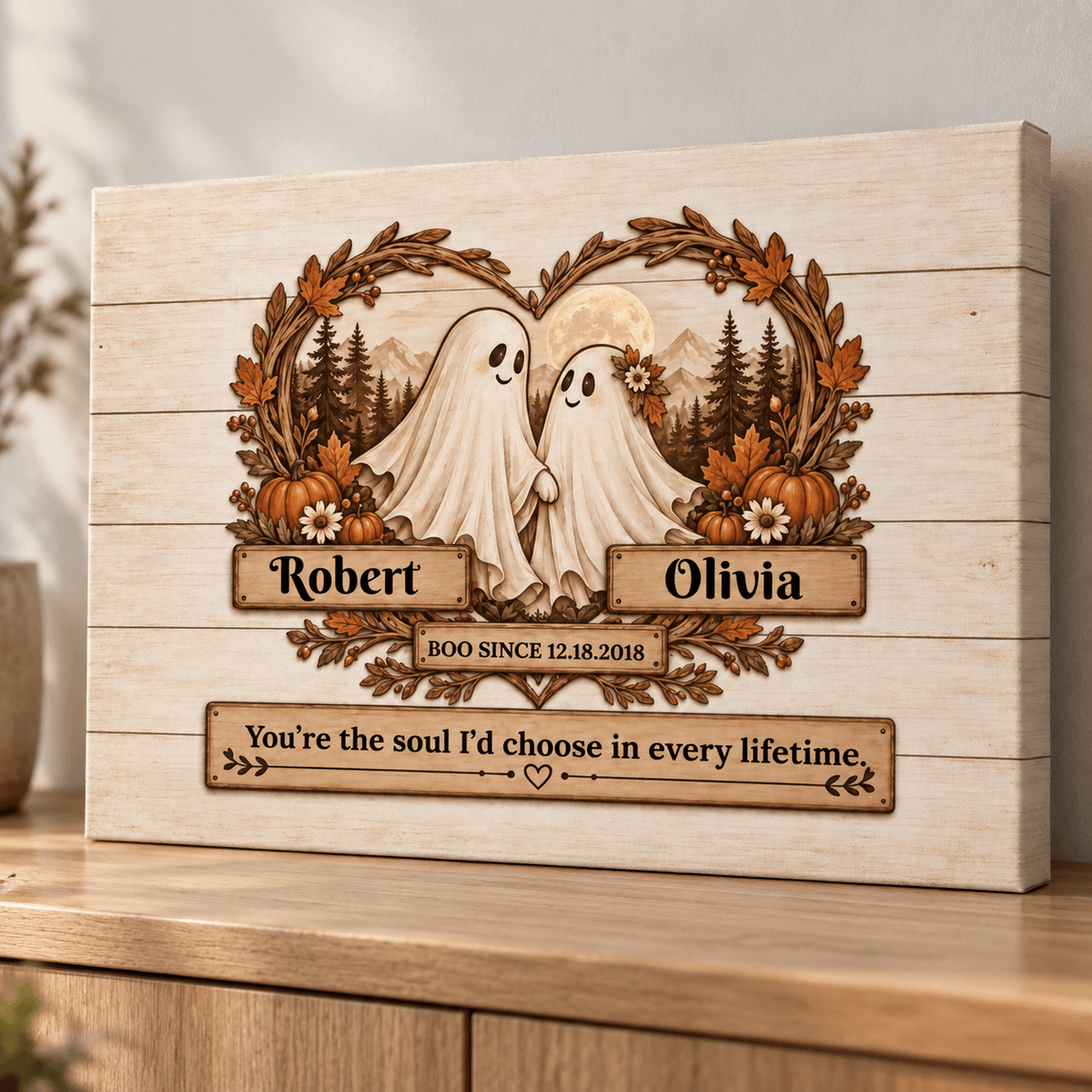 Personalized wooden Halloween wall art featuring two ghost figures inside a wreath with pumpkins, mountains, and trees, with custom names Robert and Olivia and a quote below, shown on a wooden surface.
