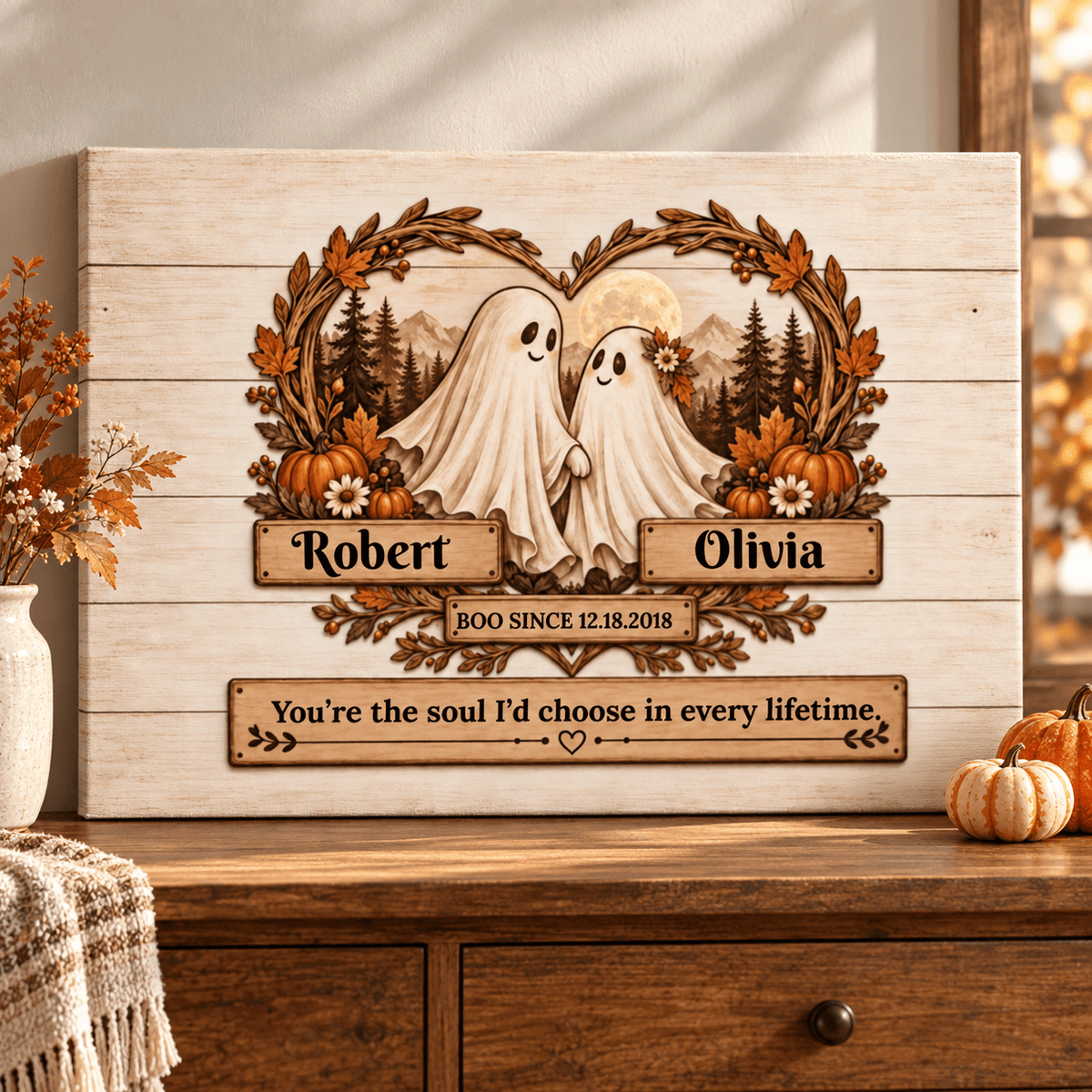 Personalized wooden sign with two smiling ghosts framed by autumn leaves and pumpkins, with the names Robert and Olivia and a memorial phrase, displayed on a wooden cabinet in a fall-themed interior.