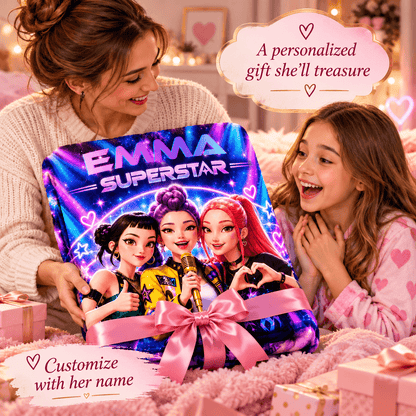 A woman and a young girl are smiling while holding a large personalized gift box featuring cartoon characters and the text 'EMMA SUPERSTAR.' The box is wrapped in a pink ribbon and bow, with cozy home decor in the background and text overlays that say 'A personalized gift she'll treasure' and 'Customize with her name.