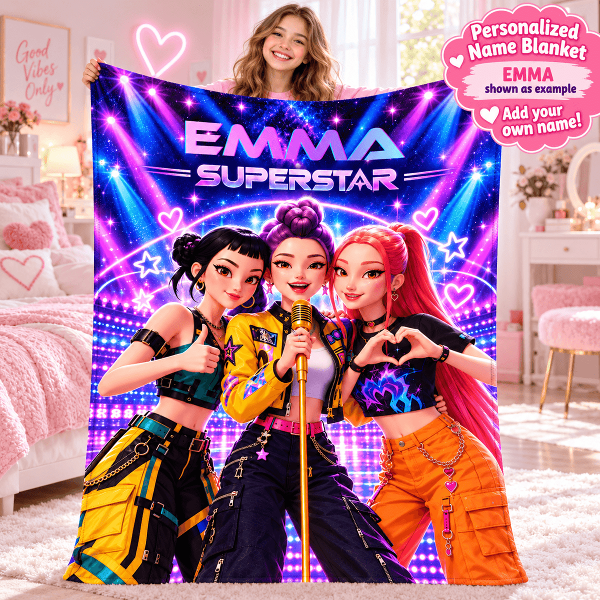 A woman holds up a large personalized name blanket featuring three cartoon-style female singers with the text 'EMMA SUPERSTAR' on a pink and purple bedroom background. A pink circular badge in the top right says 'Personalized Name Blanket EMMA shown as example Add your own name!'.