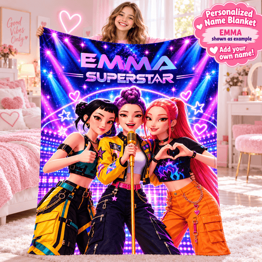 A woman holds up a large personalized name blanket featuring three cartoon-style female singers with the text 'EMMA SUPERSTAR' on a pink and purple bedroom background. A pink circular badge in the top right says 'Personalized Name Blanket EMMA shown as example Add your own name!'.