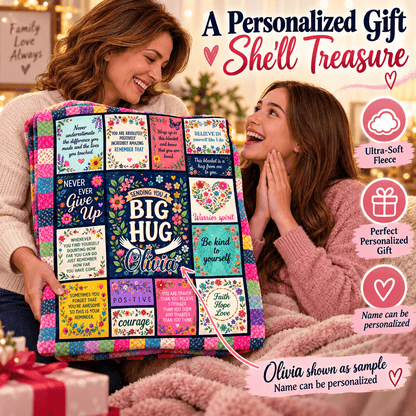 Two women smiling and hugging while holding a large personalized fleece gift blanket. The blanket features a colorful patchwork design with motivational quotes, floral patterns, and a central dark blue panel that reads 'The BIG HUG is for Olivia.