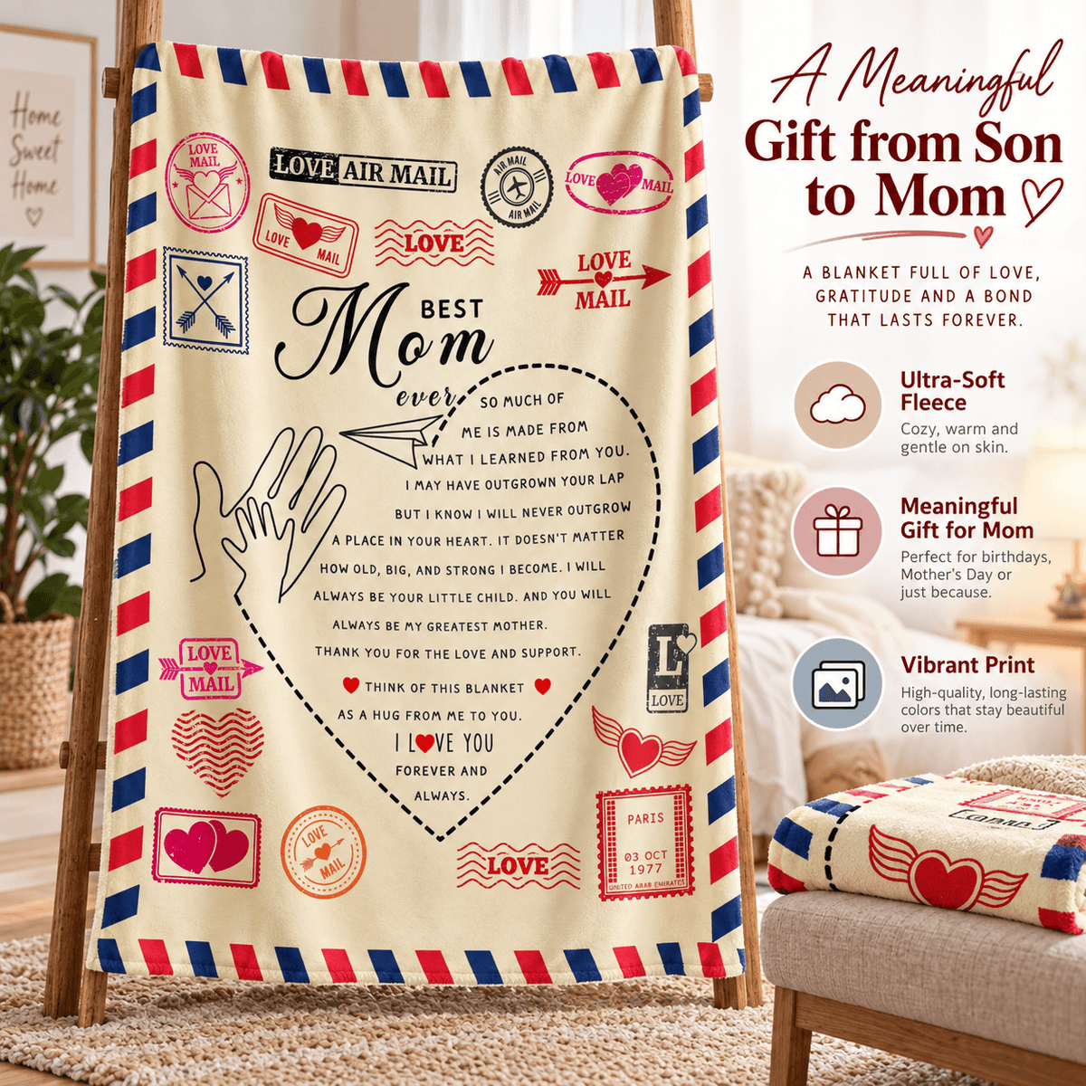A personalized Mother's Day blanket displayed on a wooden easel in a cozy living room setting. The blanket features a cream background with red and blue striped borders resembling an airmail envelope, decorated with stamps, hearts, and a central heart-shaped lettering design that reads 'Best Mom ever'.