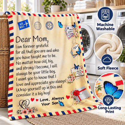 A fleece throw blanket draped over a basket in a laundry room, printed with a heartfelt letter to Mom, decorative stamps, flowers, butterflies, and a red striped border. On the right are circular callouts reading Machine Washable, Soft Fleece, and Long-Lasting Print.