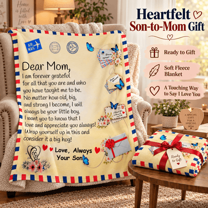 A cream-colored fleece blanket with a red and blue striped border, printed with a heartfelt letter to Mom, butterflies, postmarks, and hearts. The blanket is draped over an armchair in a cozy living room setting, with a smaller folded version on a wooden table next to it.