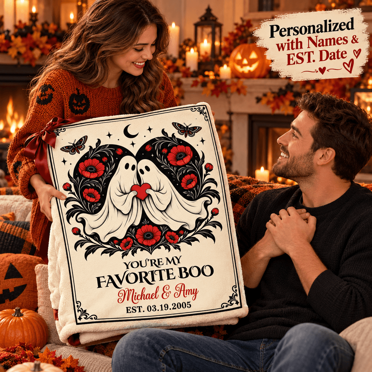 A couple in a cozy, decorated living room holds a personalized Halloween blanket. The blanket features a white background with a black and red gothic design of two ghosts surrounded by red poppies, with the text 'YOU'RE MY FAVORITE BOO' and personalized names 'Michael & Amy' and an estimated date.