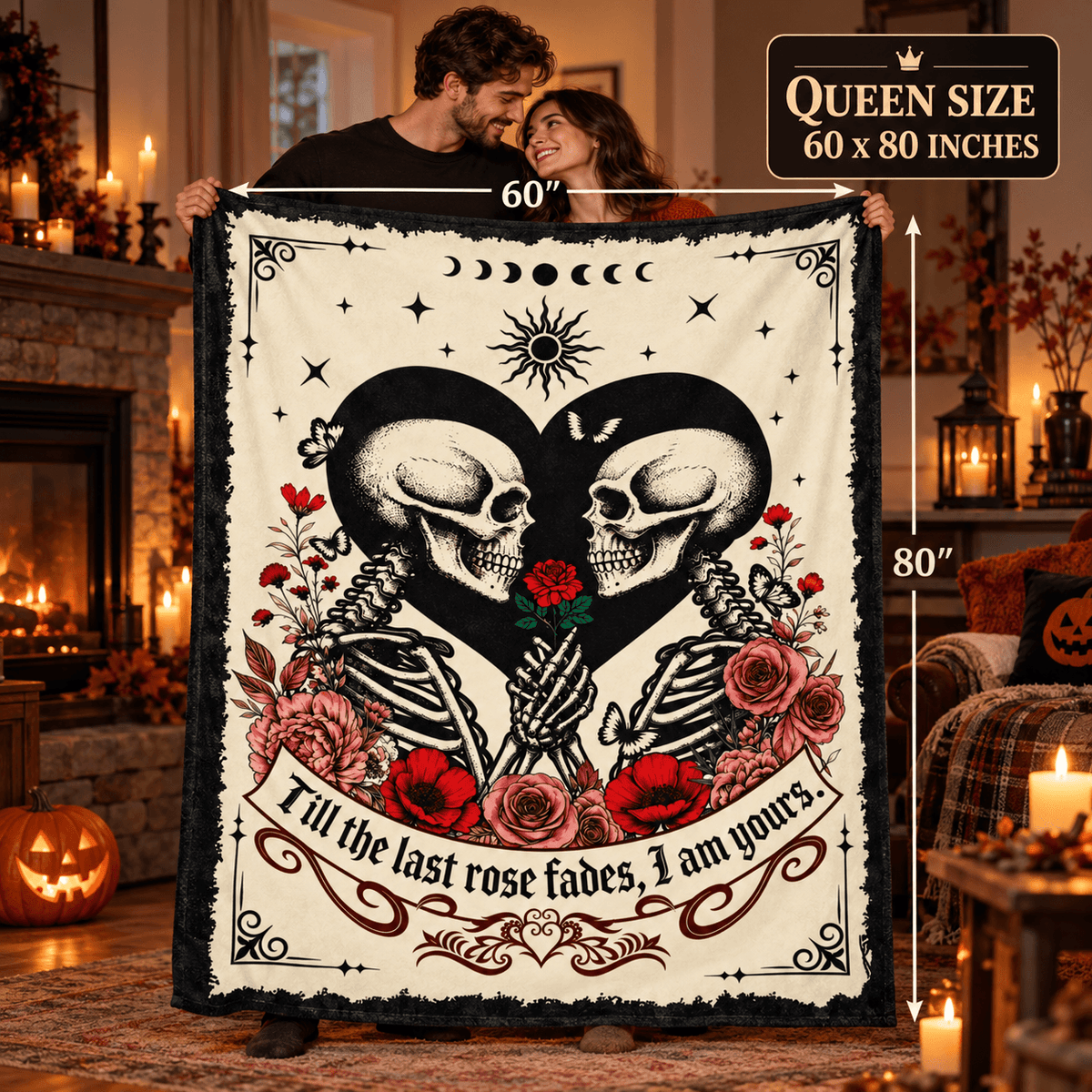 A couple holds up a large Halloween-themed fleece blanket in a cozy living room. The blanket features a cream background with a black and white skeleton design forming a heart, red roses, and the text 'I'll till the last rose fades, I am yours'.