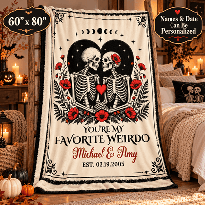 A personalized Halloween-themed fleece blanket displayed in a cozy bedroom setting. The blanket features a cream background with a black and white skeleton illustration kissing under a black moon heart, surrounded by red poppies and a red heart.