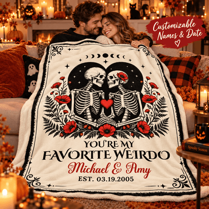A couple hugging while wrapped in a large personalized blanket featuring two skeletons, red flowers, moon phases, and the text 'YOU'RE MY FAVORITE WEIRDO Michael & Amy EST. 03.