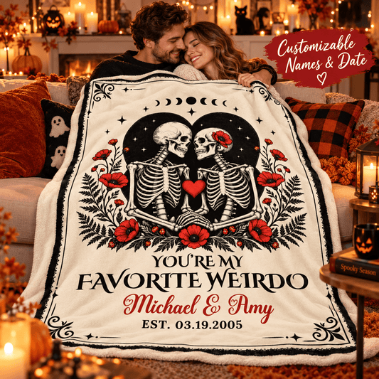 A couple hugging while wrapped in a large personalized blanket featuring two skeletons, red flowers, moon phases, and the text 'YOU'RE MY FAVORITE WEIRDO Michael & Amy EST. 03.