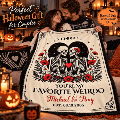 A couple hugging while holding up a personalized Halloween blanket in a cozy, warmly lit living room. The blanket features a black and white skeleton illustration with red poppies and text reading 'YOU'RE MY FAVORITE WEIRDO Michael & Amy EST.