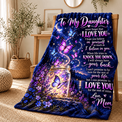 A cozy throw blanket draped over a wooden chair in a styled living room. The blanket features a deep blue background with a glowing mason jar, purple and blue butterflies, and a printed sentimental message for a daughter titled 'To My Daughter'.