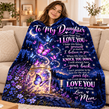 A woman wrapped in a cozy blanket while sitting on a couch in a living room. The blanket features a printed design with a glowing mason jar, purple butterflies, and a starry night sky with the text 'To My Daughter never forget that I LOVE YOU .