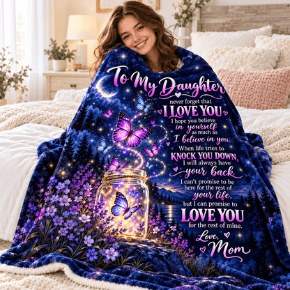A woman sitting on a bed wrapped in a blue and purple fleece blanket printed with a sentimental message for her daughter, featuring butterflies, a glowing mason jar, and floral designs.
