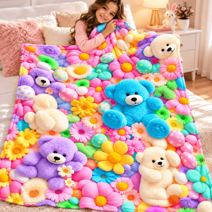 A woman lies on a bed covered with a colorful plush blanket featuring large teddy bears and bright flowers. The blanket has a multicolor design with pink, blue, yellow, purple, green, and white elements, and the room setting includes a bedside table and lamp.